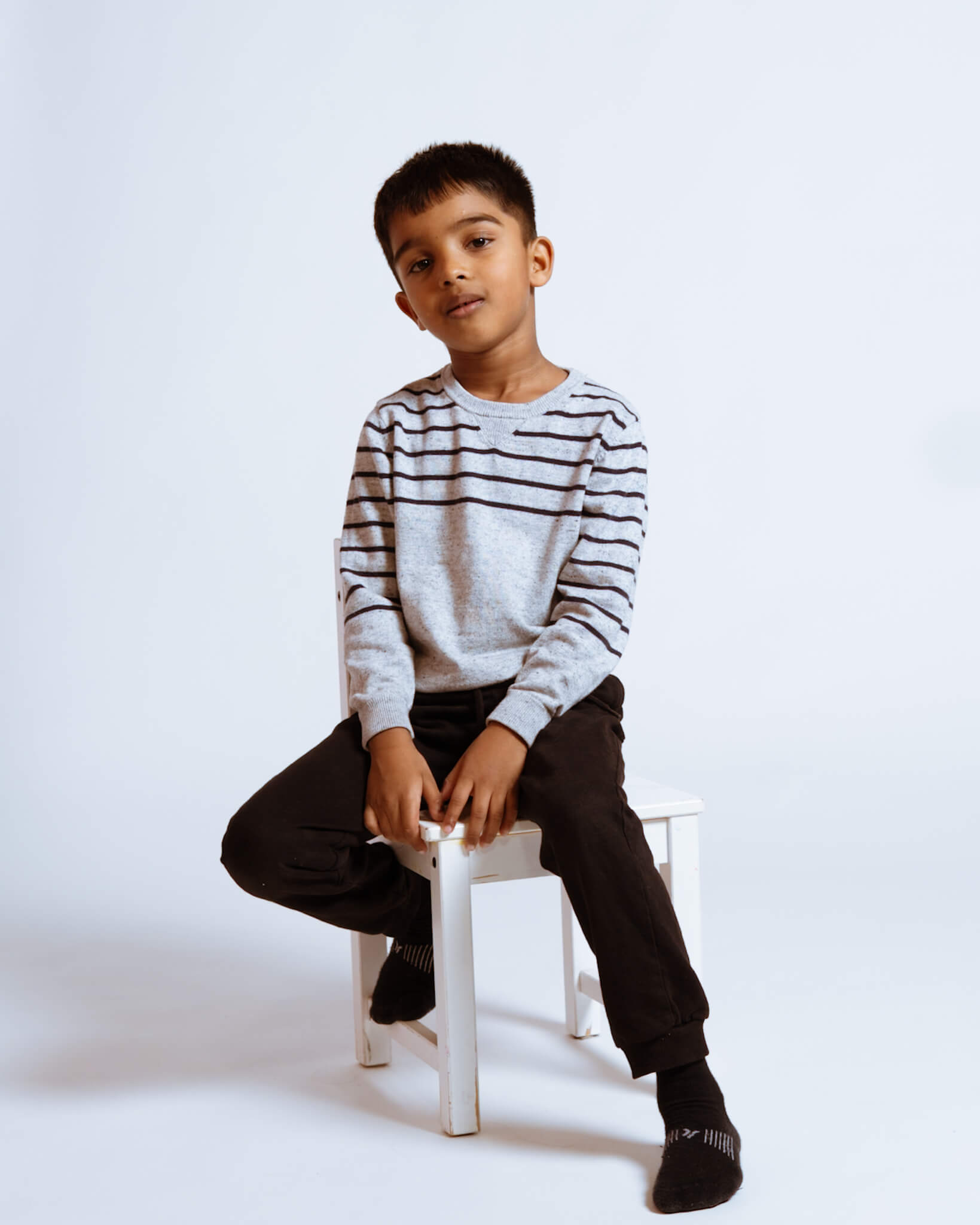 A young boy sitting casually on a white stool in Waterloo studio