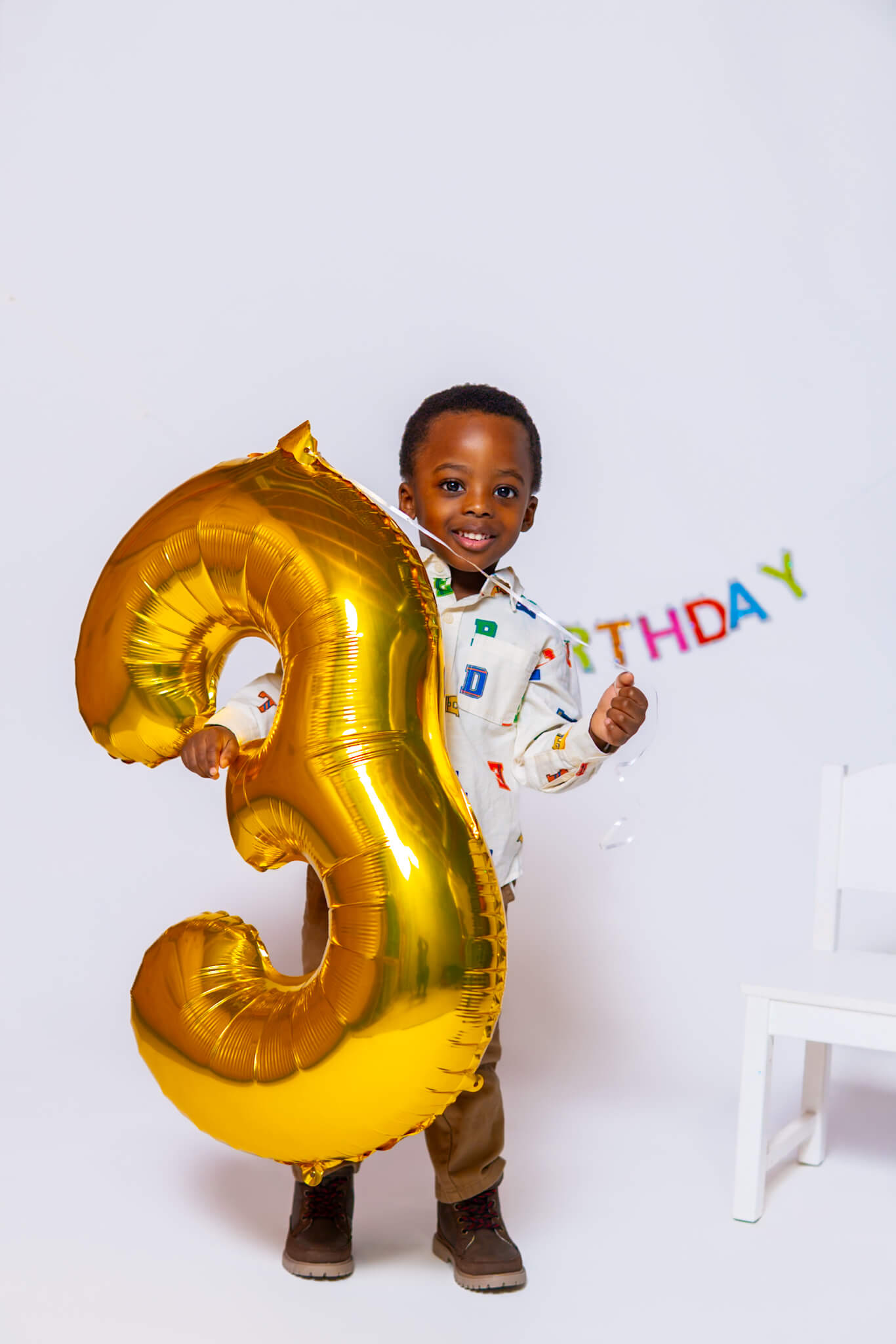 Toddler holding a large gold number three balloon for birthday photoshoot