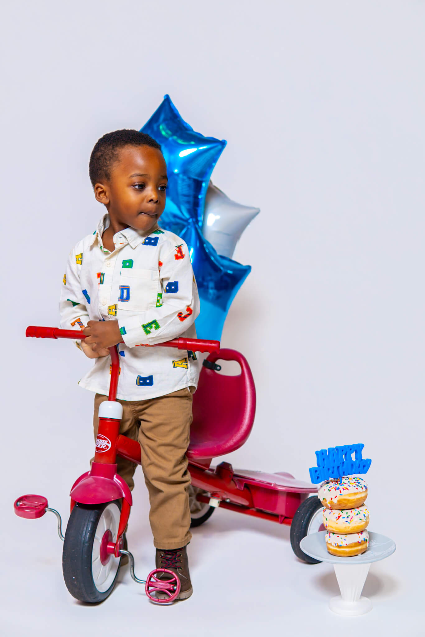 3 year old boy playing on a red tricycle during his photoshoot